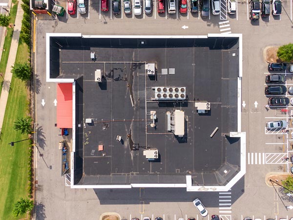 EPDM-Roofing-San-Jacinto-CA-California-2 | Woolbright's Roofing & Construction Aerial view of a flat-roof building surrounded by parked cars; rooftop HVAC units and equipment visible near the center.
